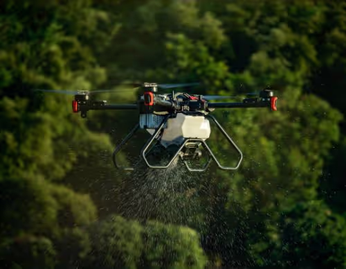 Drone spraying liquid over green foliage, surrounded by blurred dense forest background.